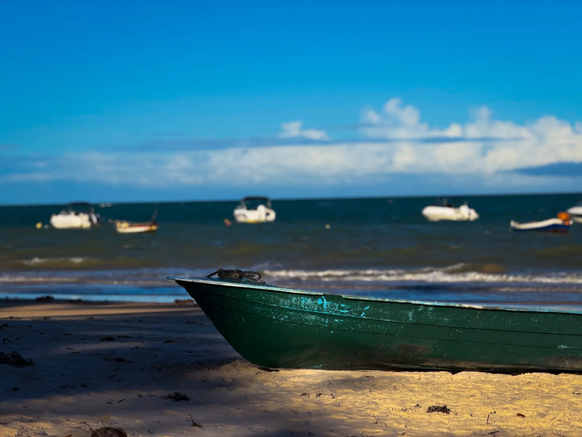 Canoa verde na areia com barcos ancorados no mar ao fundo